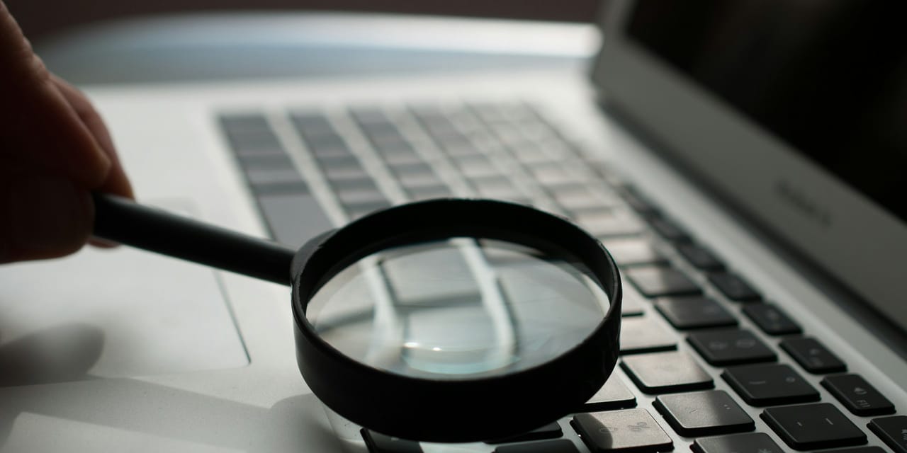 Lupa asezata peste tastatura unui laptop, ca simbol al verificarii intr-un registru public